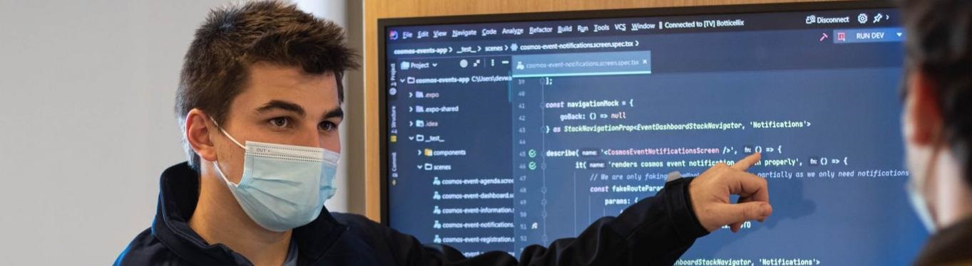 Man in face covering pointing at computer screen of code