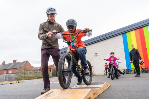 Ed Clancy and a pupil of Goldthrope primary academy scooting on a portable street ramp
